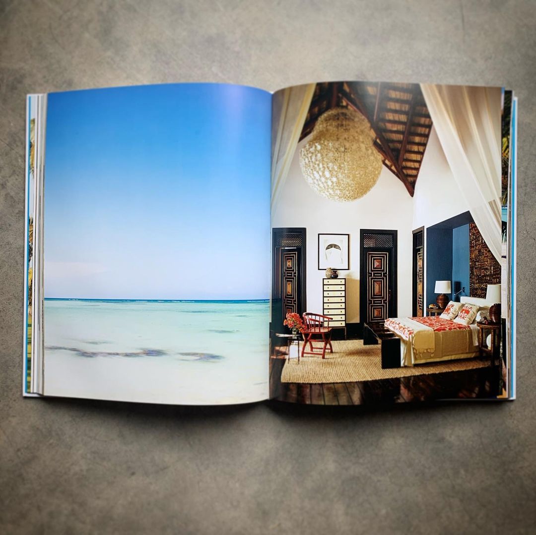 Open book displays a serene beach scene alongside a cozy bedroom interior featuring a bed, dresser, artwork, and decorative lighting.
