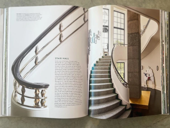 Image of a magazine spread featuring a grand stair hall with curved staircase, neutral decor, and distinctive architectural details.