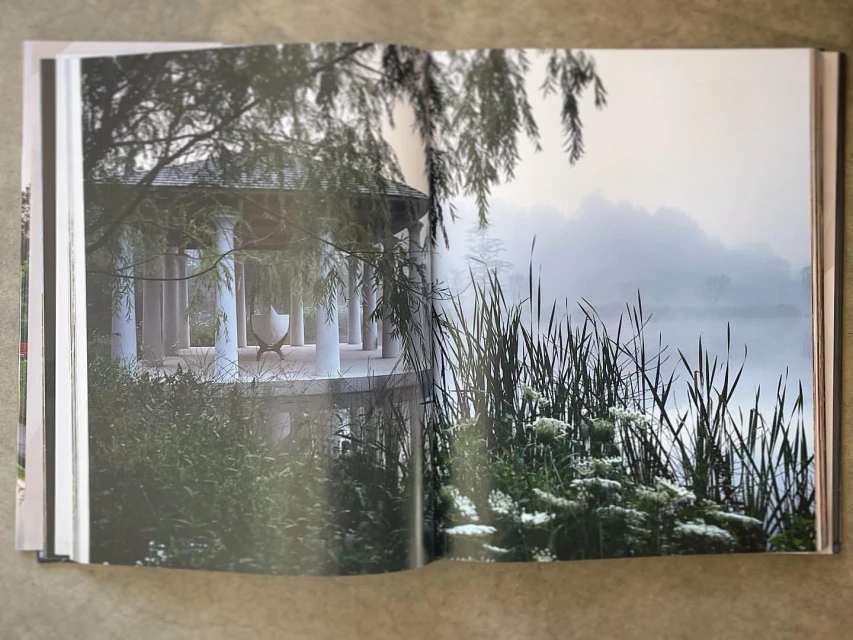 Open book displaying a photograph of a gazebo with white columns by a foggy lake surrounded by greenery, creating a serene outdoor scene.