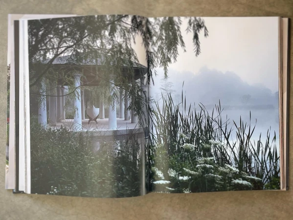 Open book displaying a photograph of a gazebo with white columns by a foggy lake surrounded by greenery, creating a serene outdoor scene.