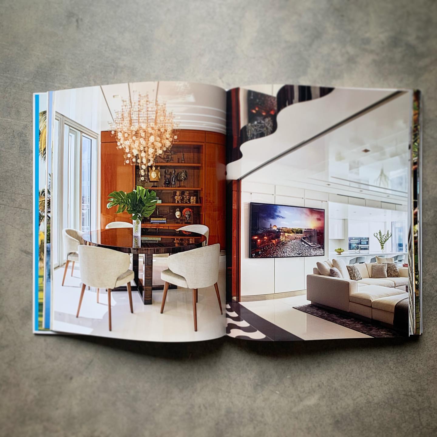 Open magazine spread showing modern interior design with dining table and living area, featuring a chandelier, white walls, and hardwood elements.