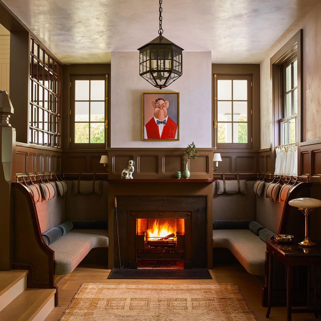 Warm, inviting interior showcases a fireplace, gray upholstered seating, and a whimsical portrait in a room with wood paneling.