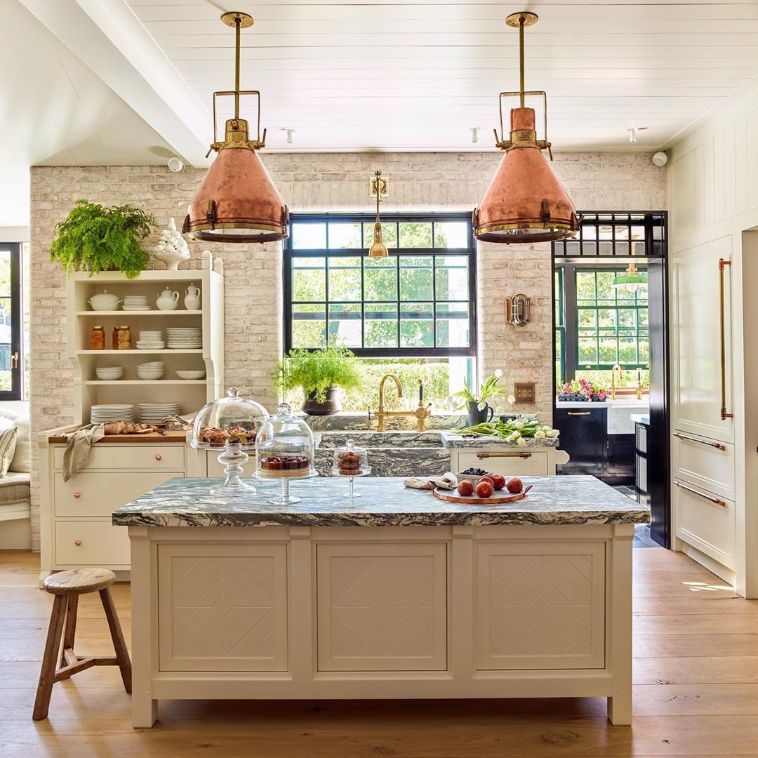 Bright, airy kitchen with island, copper pendant lights, and white brick walls. Green plants add a touch of nature to the interior.