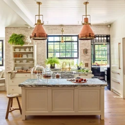 Bright kitchen interior featuring a marble island, white cabinetry, and two large copper pendant lights hanging overhead.