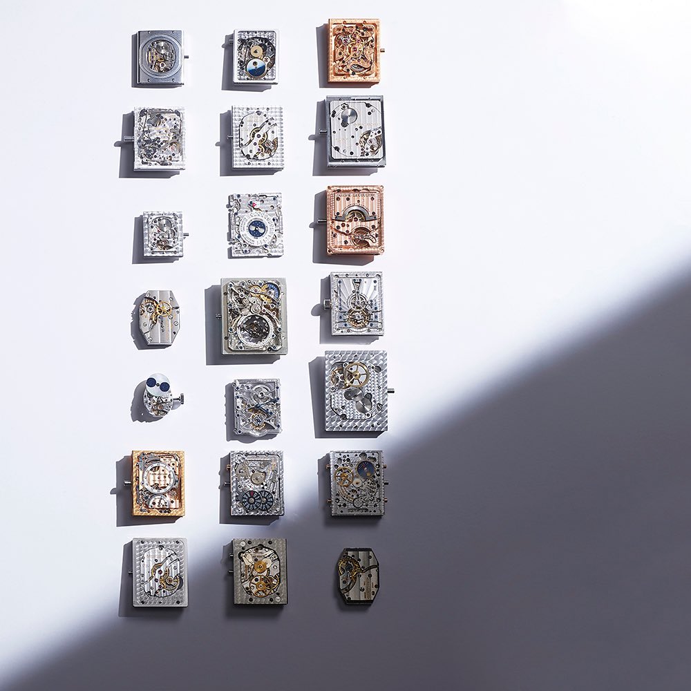 Overhead shot of a grid of rectangular objects with gears and clockwork elements, presented on a white surface with shadow.