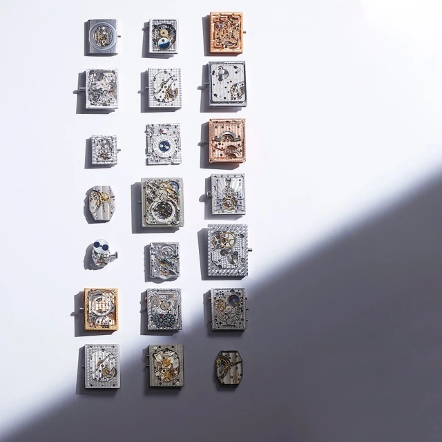 Overhead shot of a grid of rectangular objects with gears and clockwork elements, presented on a white surface with shadow.