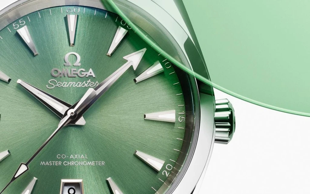 Close-up shot of an Omega Seamaster wristwatch with a green dial and silver hands, featuring the Omega logo and a domed crystal.