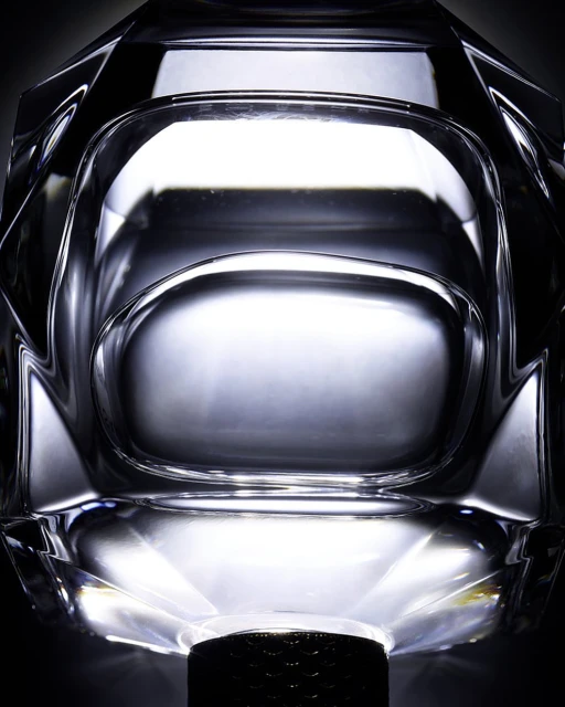 Close-up of a crystal glass object with faceted details, showcasing a transparent material and its geometric form against a dark background.