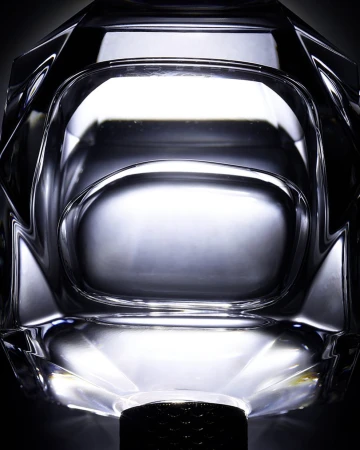 Close-up of a crystal glass object with faceted details, showcasing a transparent material and its geometric form against a dark background.