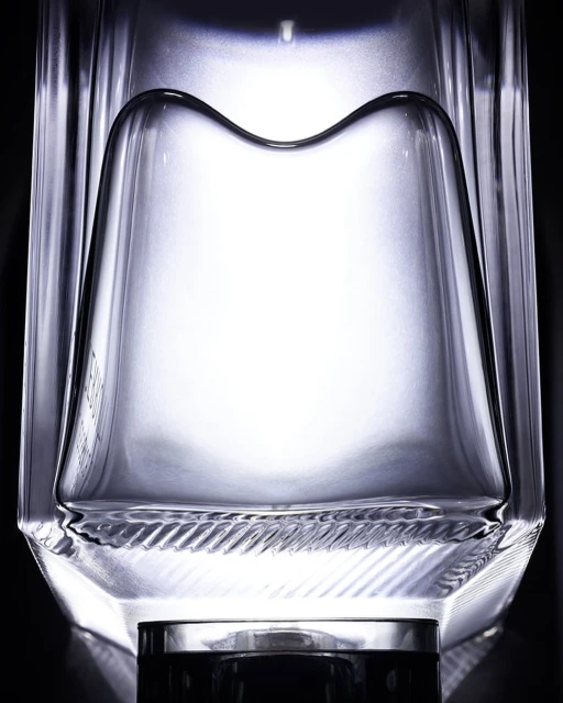 Close-up studio shot of a clear glass bottle with angular design against a dark backdrop, emphasizing its unique shape and texture.