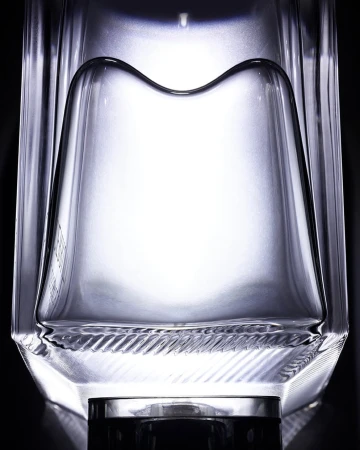 Close-up studio shot of a clear glass bottle with angular design against a dark backdrop, emphasizing its unique shape and texture.