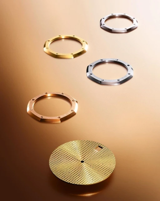 Four watch bezels and a watch face in gold, silver and bronze are arranged on a gradient brown background in a studio shot.