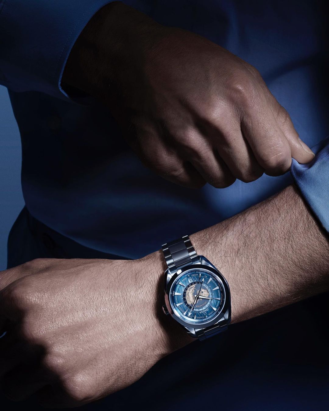 Close-up of a male wrist wearing a modern stainless steel wristwatch with blue dial, complemented by a light blue dress shirt.