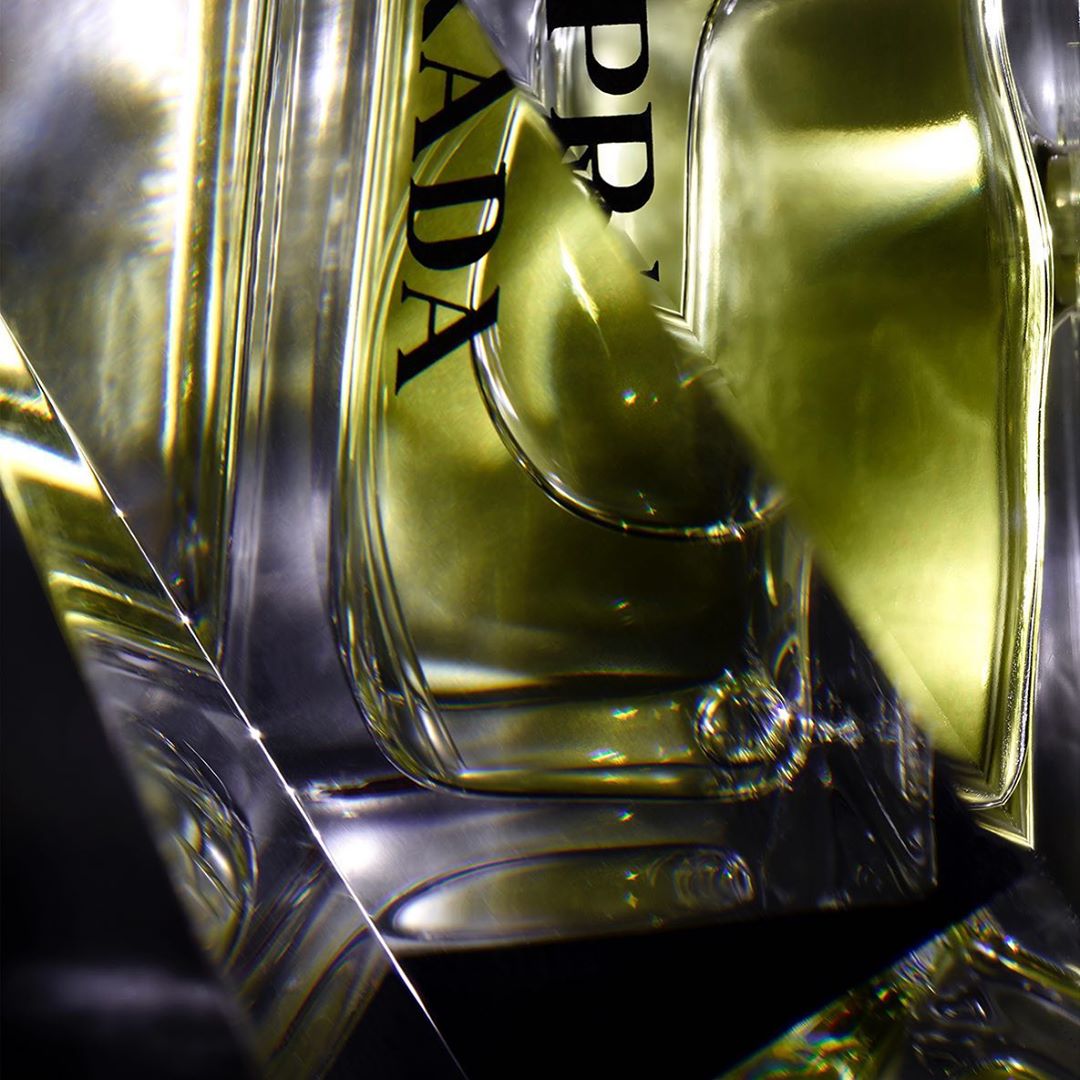 Close-up of a clear glass Prada perfume bottle with a light yellow liquid inside, highlighting its shape and the Prada label.