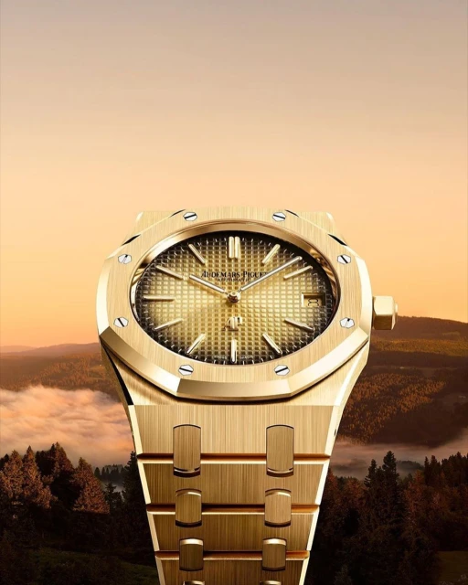 Close-up of a gold Audemars Piguet Royal Oak wristwatch with a textured dial set against a blurred background of trees and sky.