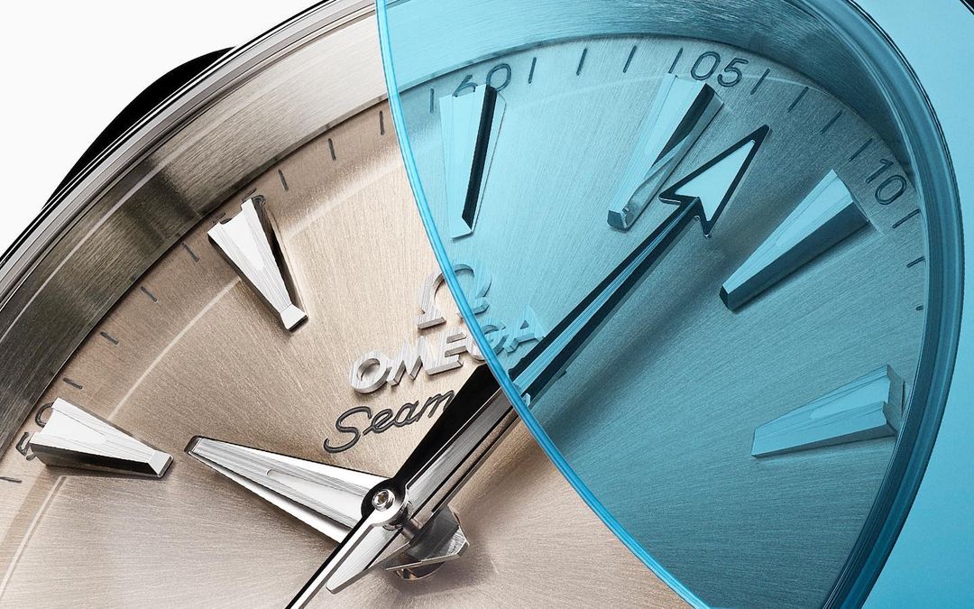 Close-up of an Omega Seamaster watch face, featuring a two-toned silver and blue metallic texture and detailed markings.