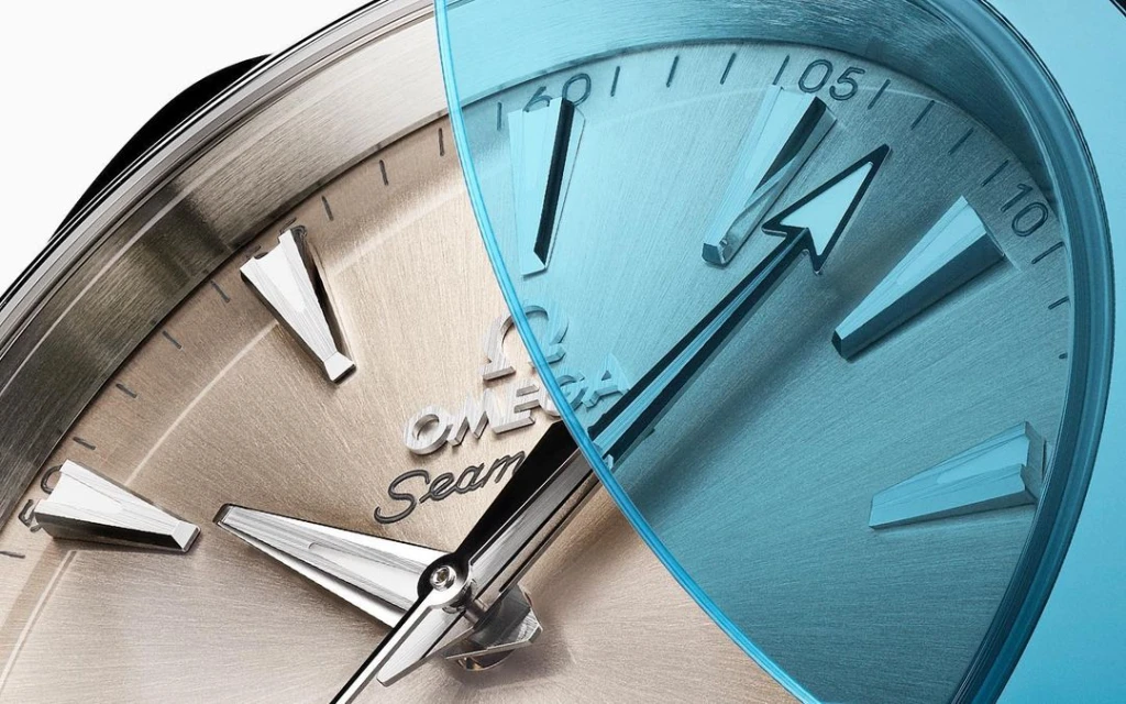 Close-up of an Omega Seamaster watch face, featuring a two-toned silver and blue metallic texture and detailed markings.