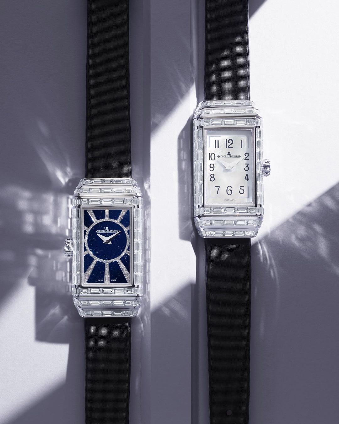 Two luxury rectangular timepieces with gemstone bezels and dark straps are displayed on a light surface with soft lighting.
