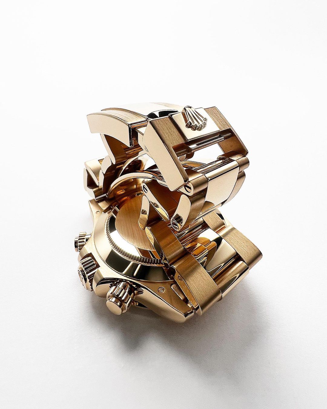 High-angle shot of a gold Rolex watch with a metal strap, showcasing its intricate design and luxurious appeal against a white backdrop.