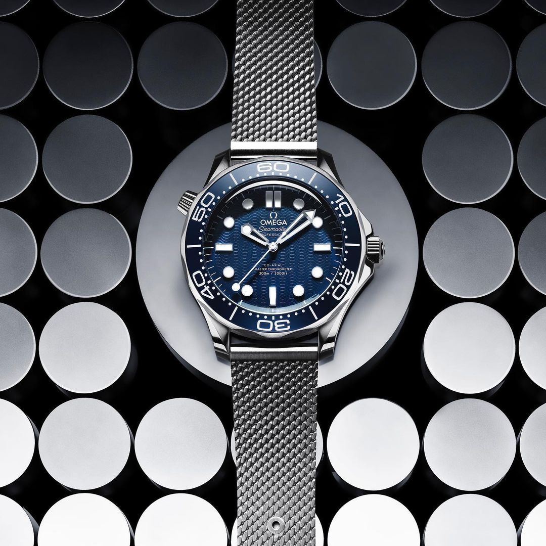 Close-up of an Omega Seamaster watch on a grey disc against a patterned background, showcasing the watch's design and metallic band.