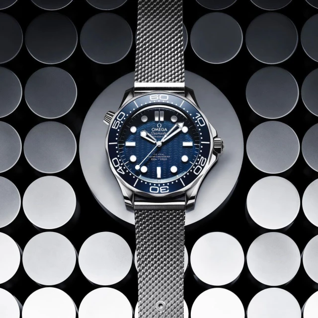 Close-up of an Omega Seamaster watch on a grey disc against a patterned background, showcasing the watch's design and metallic band.