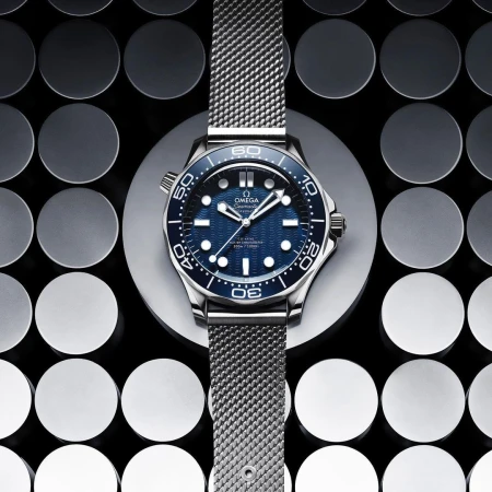 Close-up of an Omega Seamaster watch on a grey disc against a patterned background, showcasing the watch's design and metallic band.