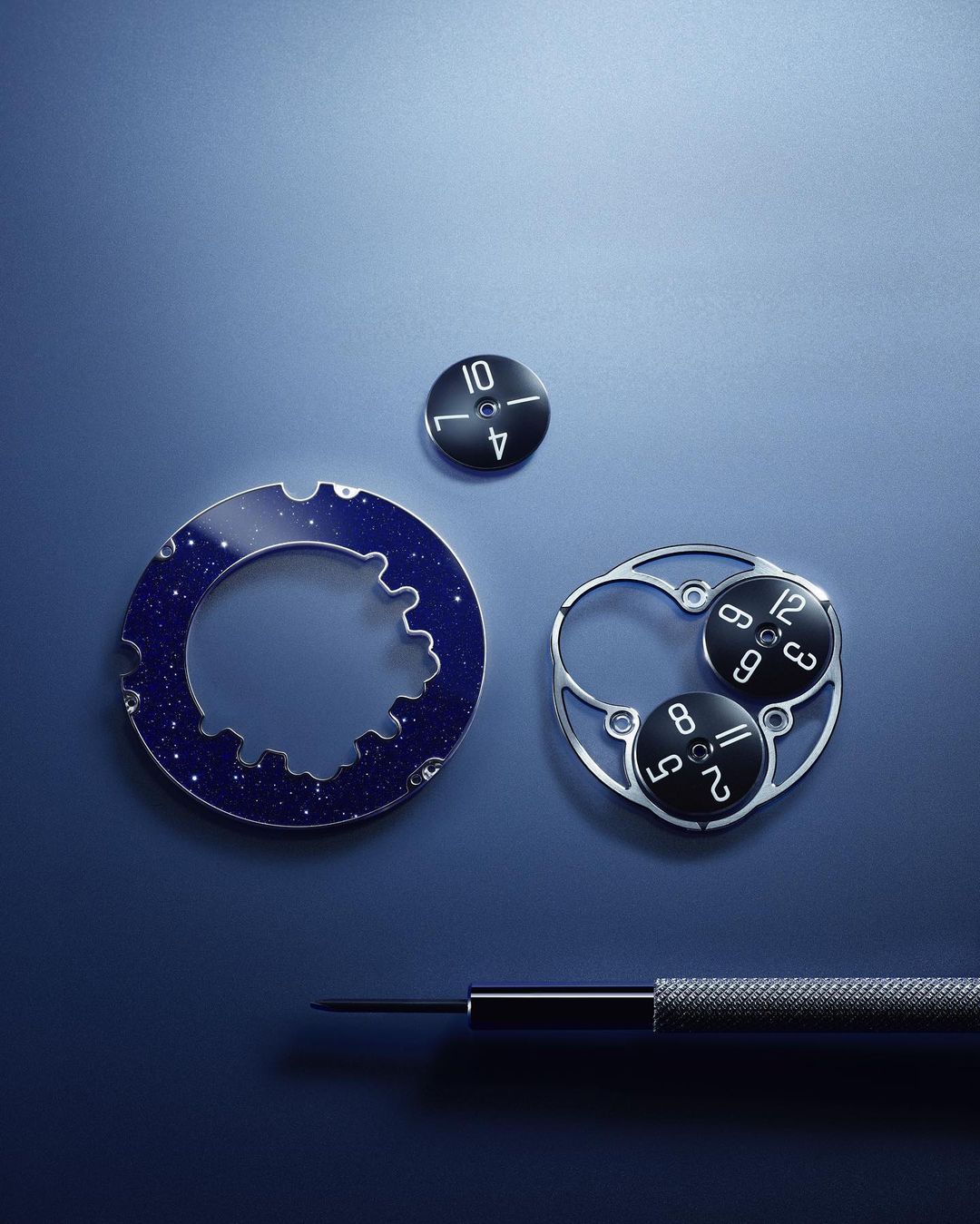 Close-up of watch parts including gears, dial components, and a small screwdriver on a blue surface, highlighting horology.