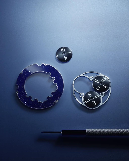 Close-up of watch parts including gears, dial components, and a small screwdriver on a blue surface, highlighting horology.