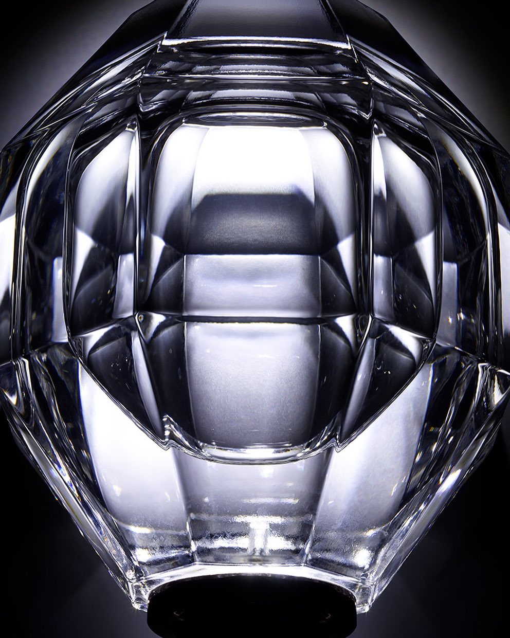 Close-up of a clear faceted glass vase with geometric design and a black base, set against a dark background, highlighting light refraction.