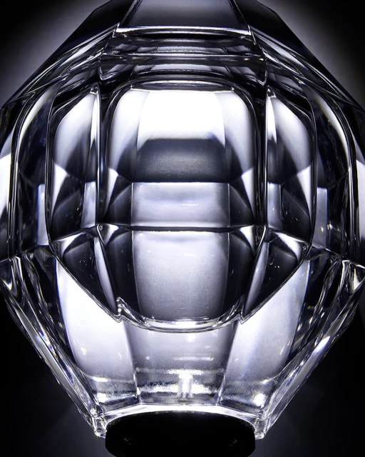 Close-up of a clear faceted glass vase with geometric design and a black base, set against a dark background, highlighting light refraction.