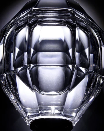 Close-up of a clear faceted glass vase with geometric design and a black base, set against a dark background, highlighting light refraction.