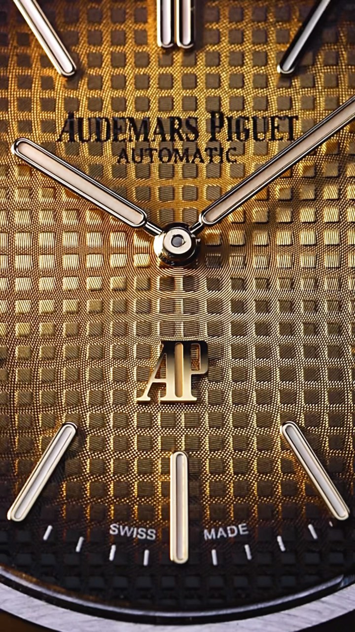 Close-up of a gold Audemars Piguet watch face with silver hands and markers, showcasing its intricate patterned texture.