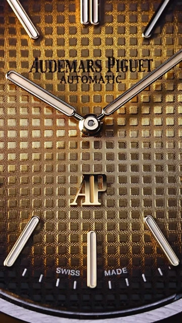 Close-up of a gold Audemars Piguet watch face with silver hands and markers, showcasing its intricate patterned texture.