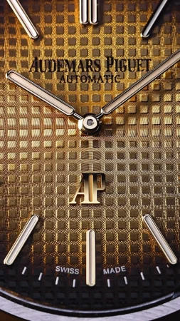 Close-up of a gold Audemars Piguet watch face with silver hands and markers, showcasing its intricate patterned texture.