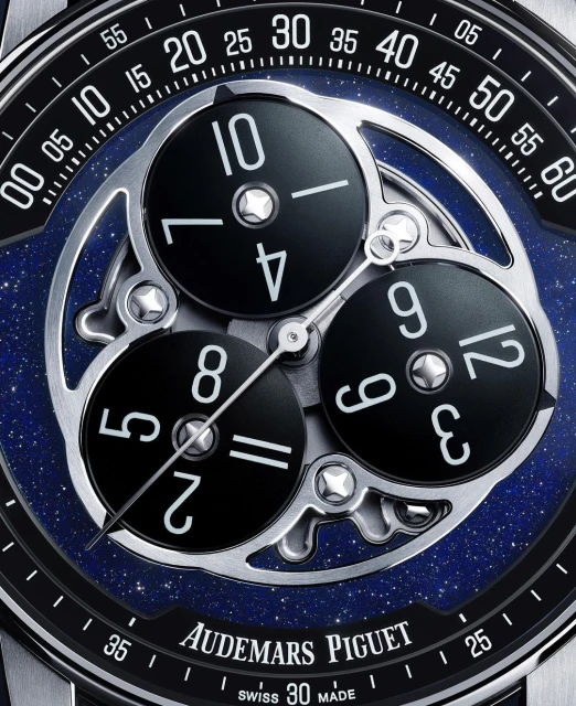 Close-up of an Audemars Piguet watch face with multiple dials and silver mechanics against a blue and black speckled background.