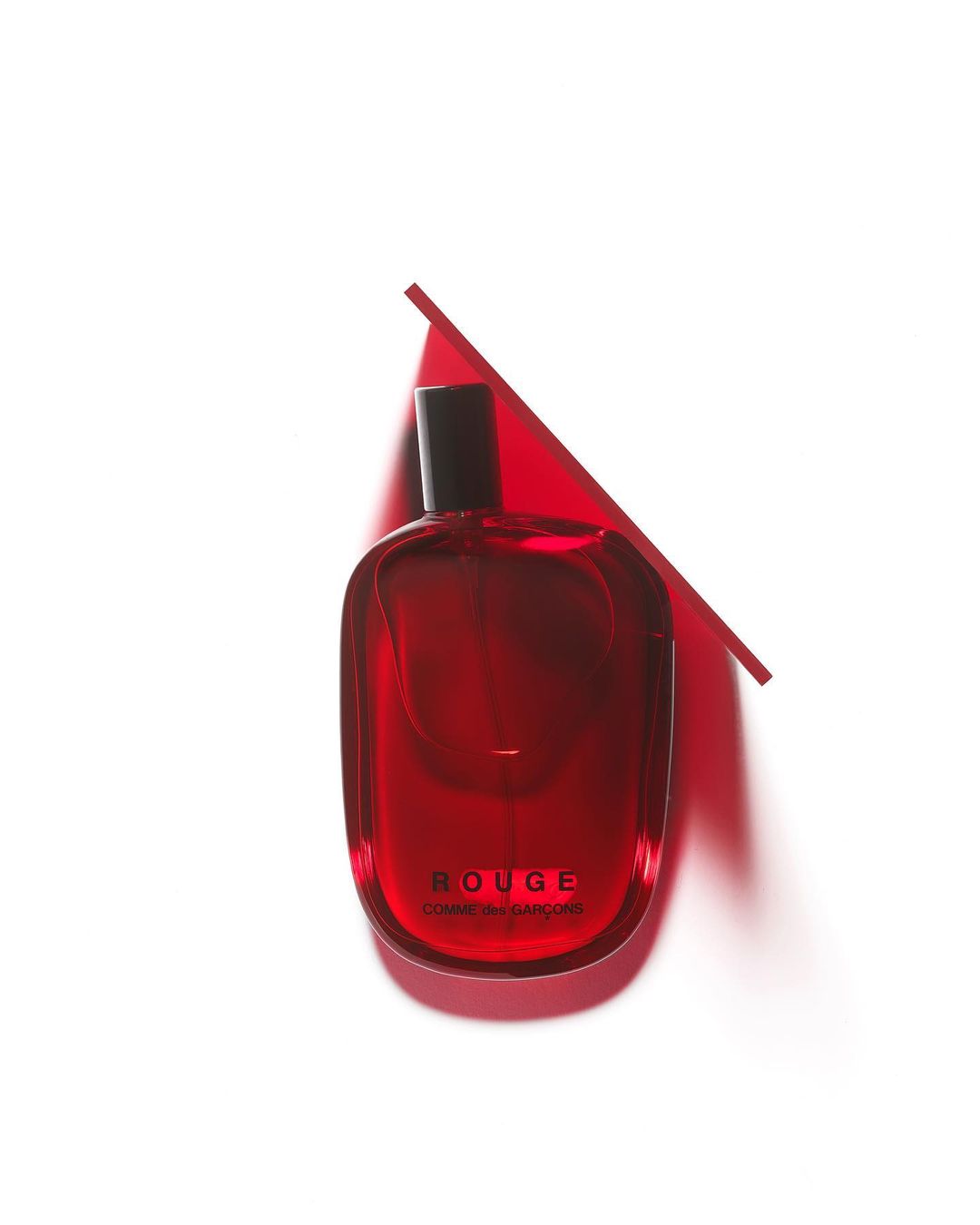 Red perfume bottle by Comme des Garçons with a geometric red accent against a white backdrop, showcasing beauty and fragrance.