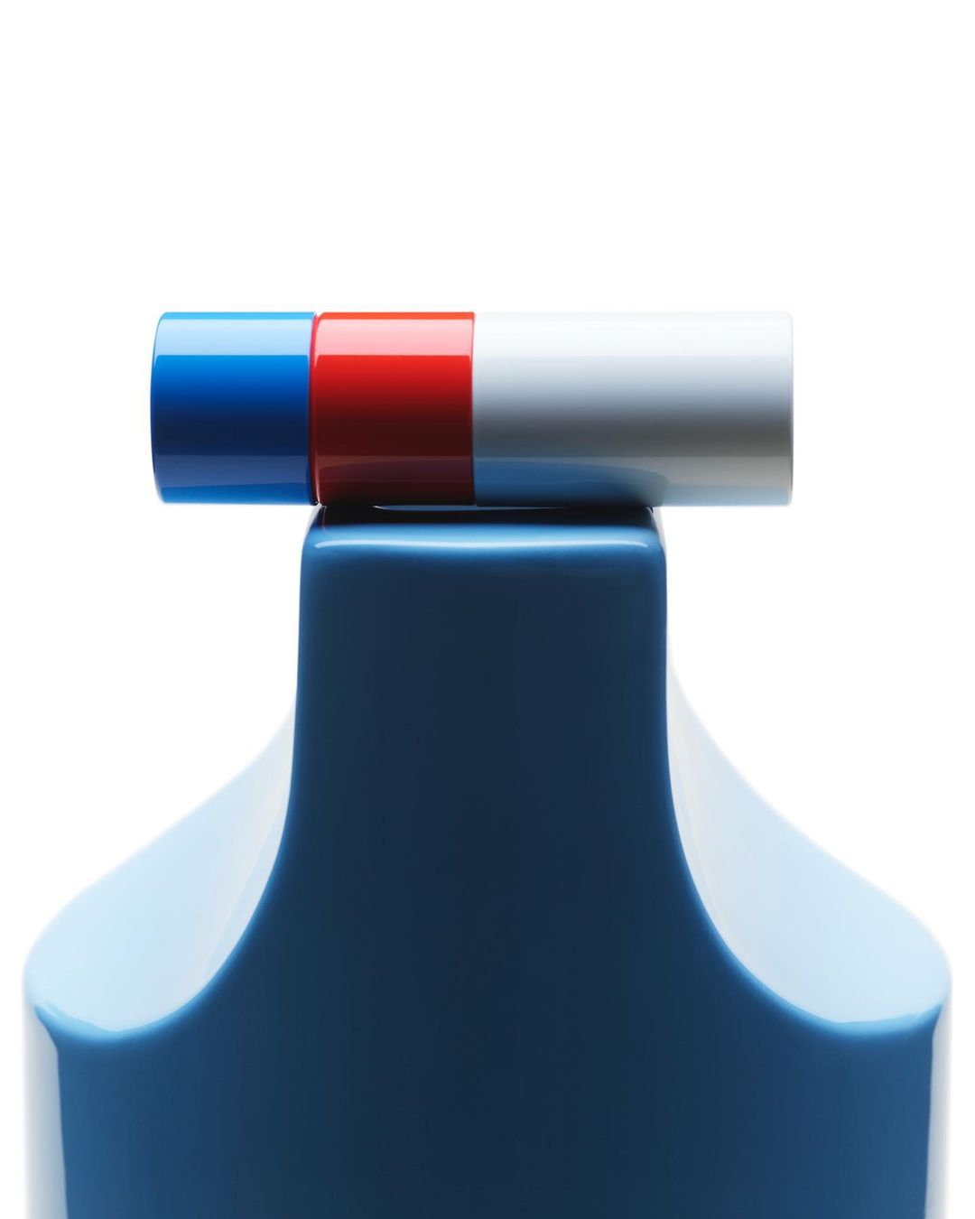 Close-up of a blue bottle base topped by a horizontal cylinder divided into blue, red, and white sections against a white backdrop.