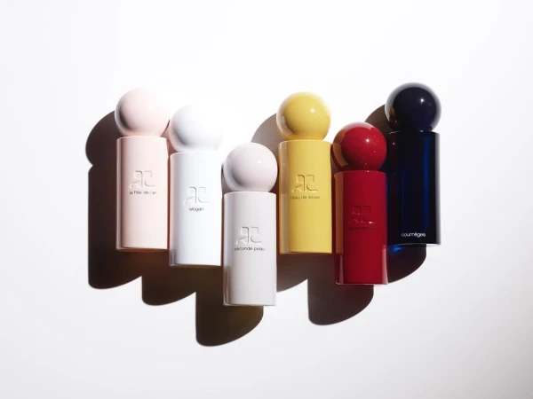 Collection of colorful Courreges perfume bottles in pink, white, yellow, red, and blue, lined up on a white surface with shadows.