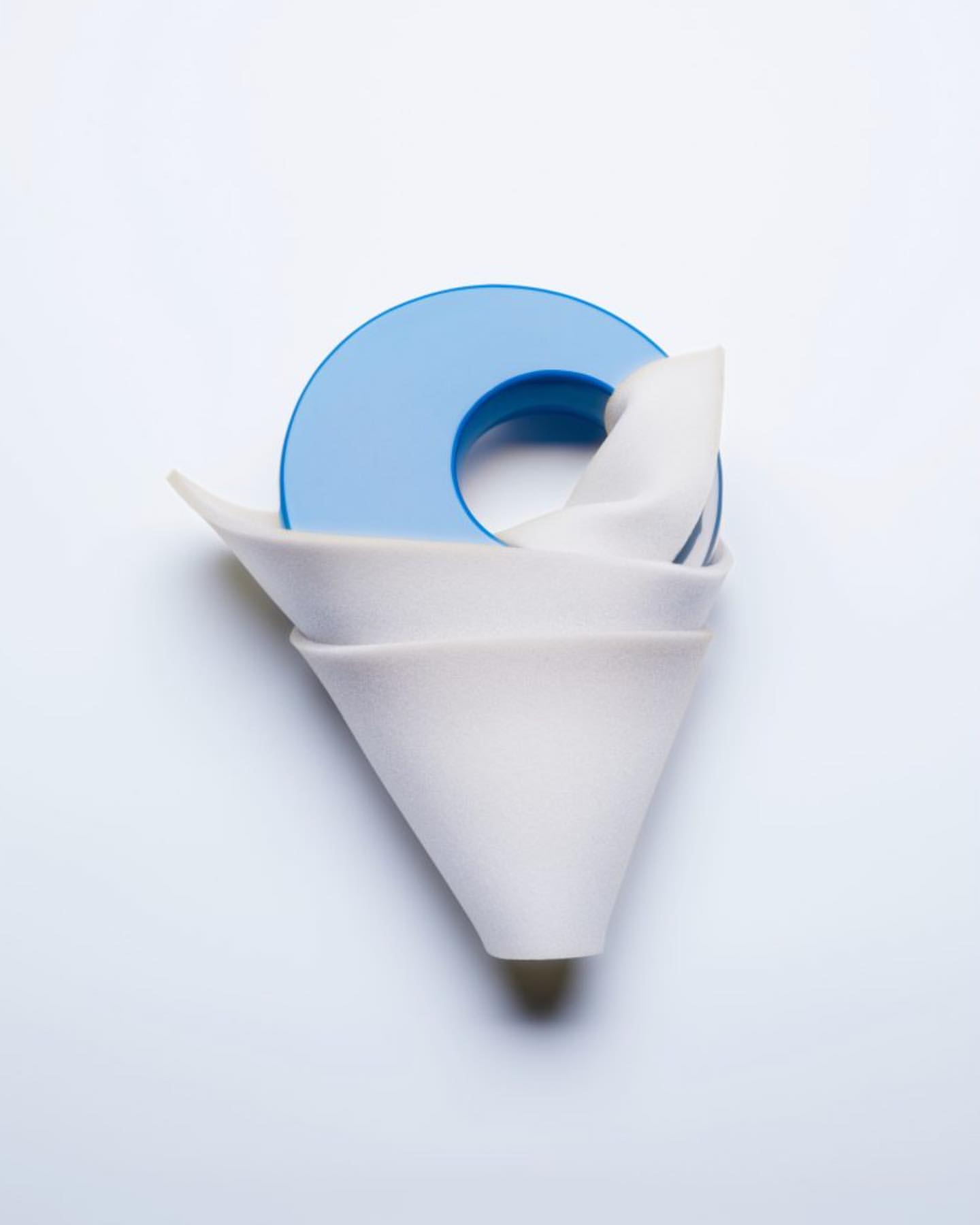 Still life photograph of stacked white ceramic coffee filters with a blue plastic holder on a white background, studio lighting.