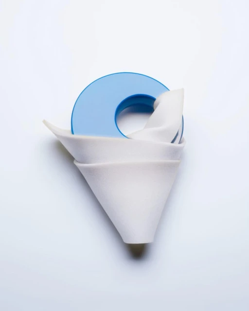 Still life photograph of stacked white ceramic coffee filters with a blue plastic holder on a white background, studio lighting.