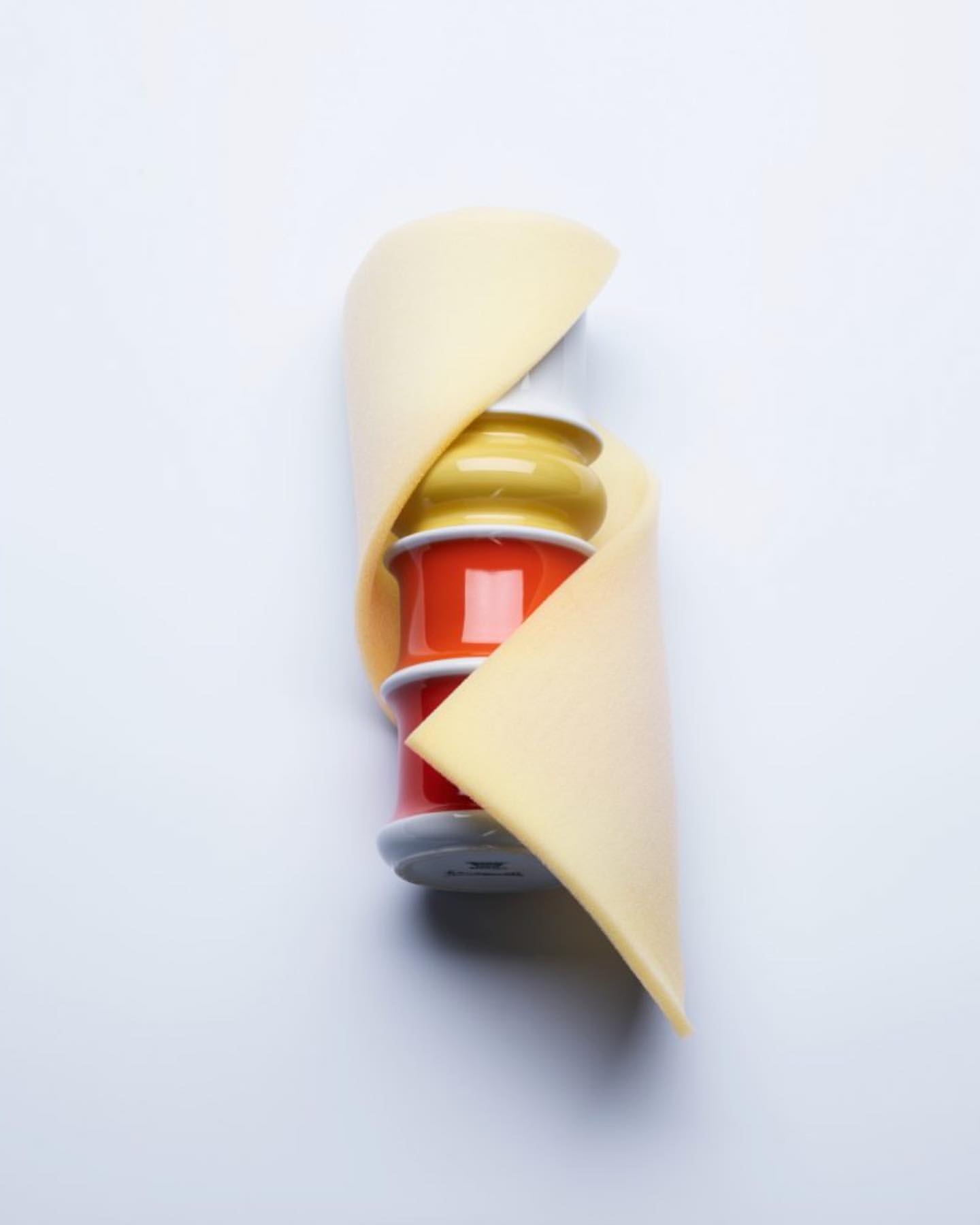 Still life shot of stacked colorful thread spools wrapped with a light yellow swatch of fabric on a plain white background.