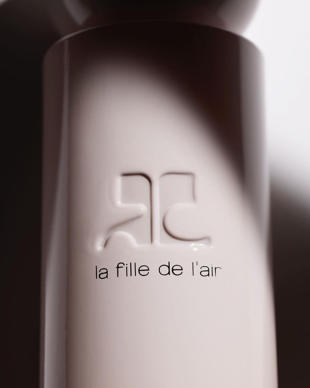 Close-up studio shot of a cream-colored fragrance bottle featuring an embossed logo and 'la fille de l'air' text.