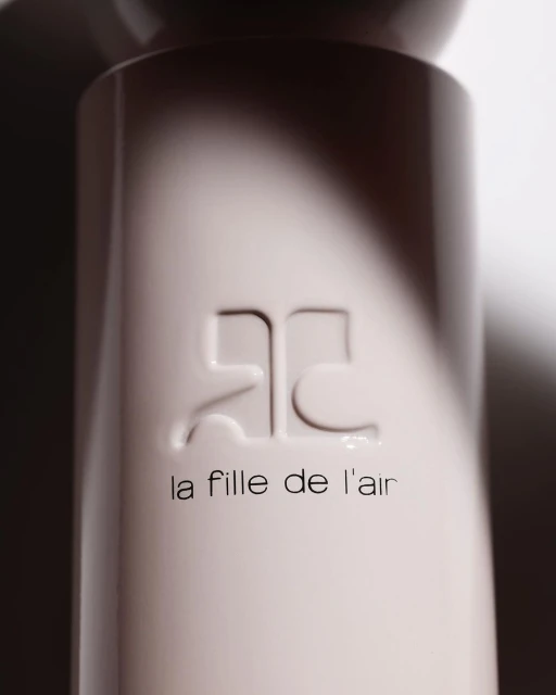 Close-up studio shot of a cream-colored fragrance bottle featuring an embossed logo and 'la fille de l'air' text.