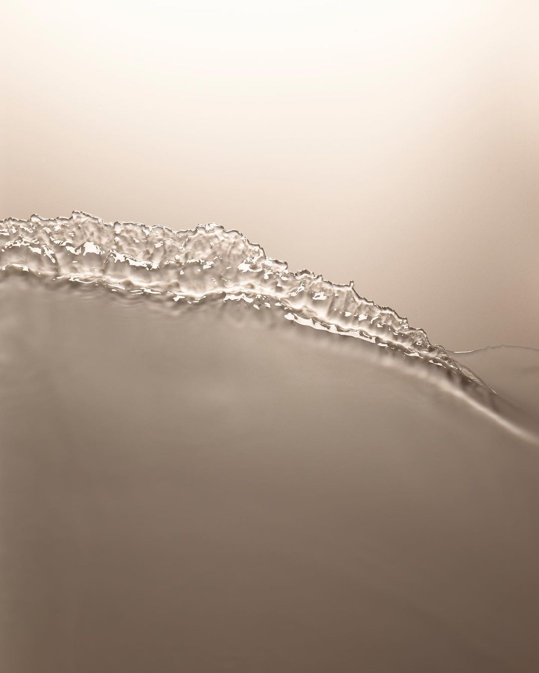 Abstract photograph of neutral-toned liquid surface with textured, crystallized edge, creating a minimalistic yet visually intriguing composition.