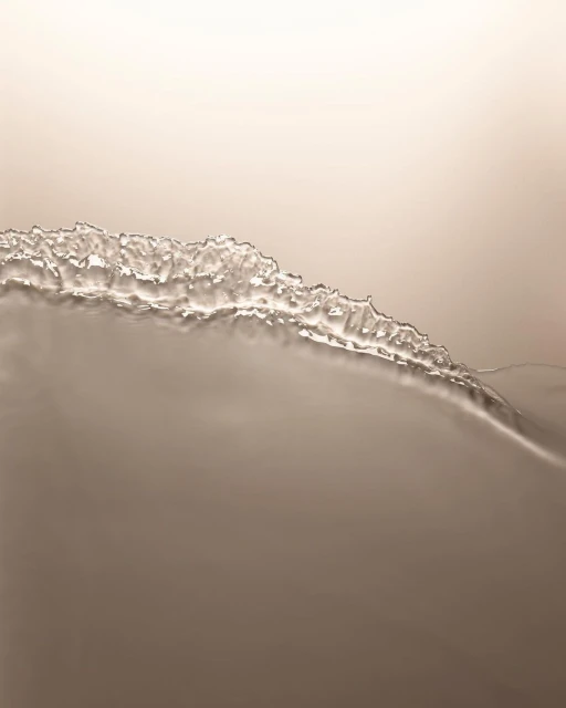 Abstract photograph of neutral-toned liquid surface with textured, crystallized edge, creating a minimalistic yet visually intriguing composition.