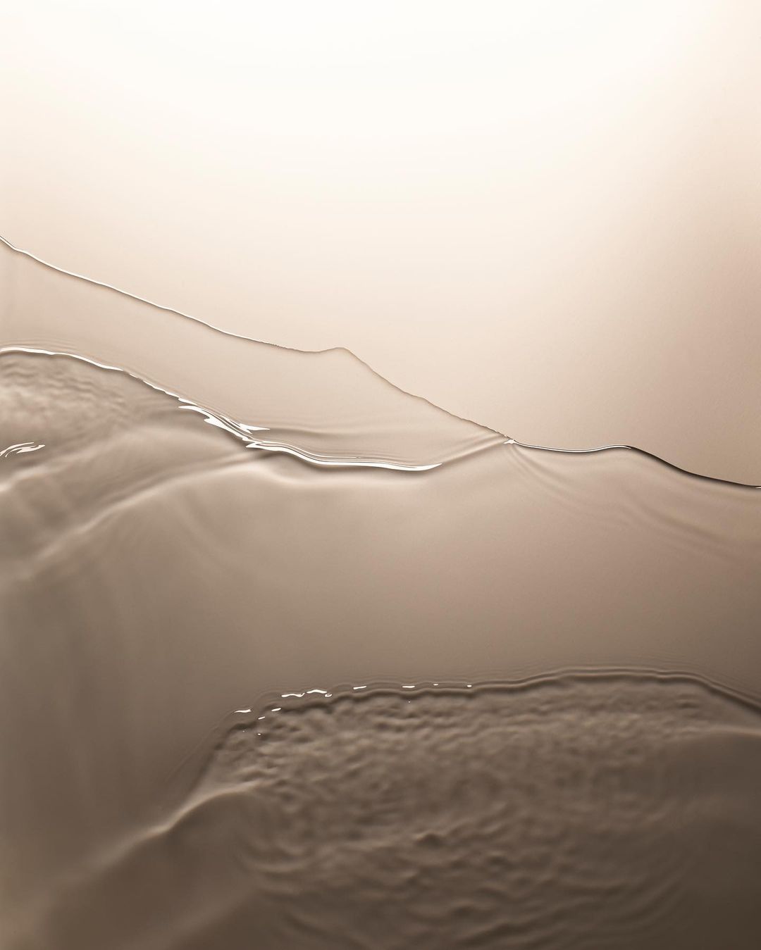Abstract image of liquid with a glossy surface, featuring warm, neutral tones with textured ripples and a gradient background.