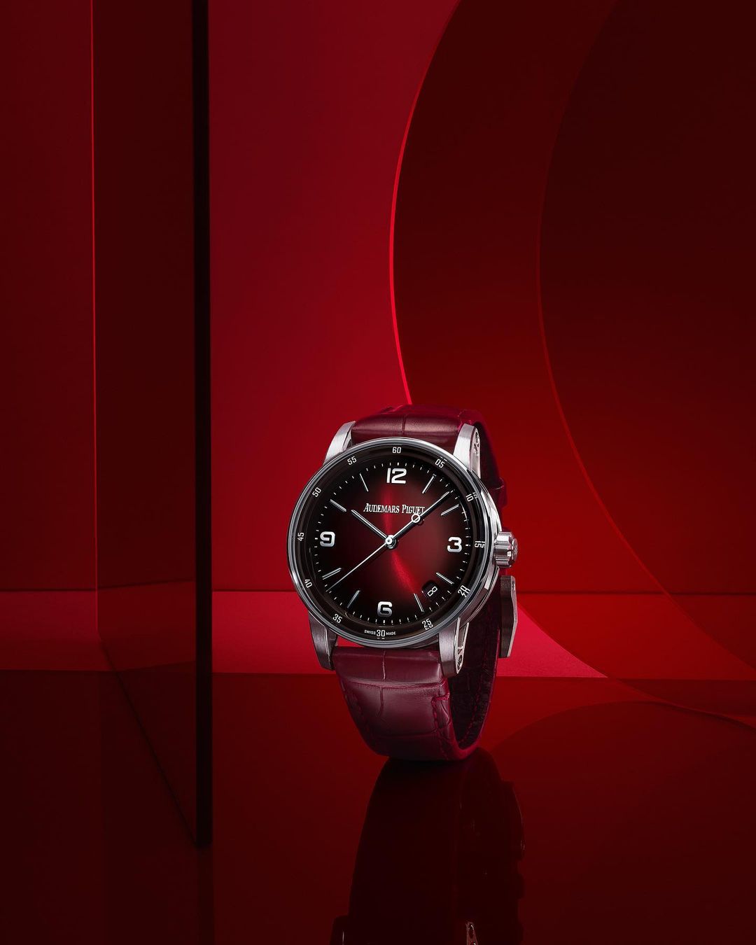 Audemars Piguet wristwatch on a reflective surface, with a red dial and a red leather strap, against a red background with geometric shapes.