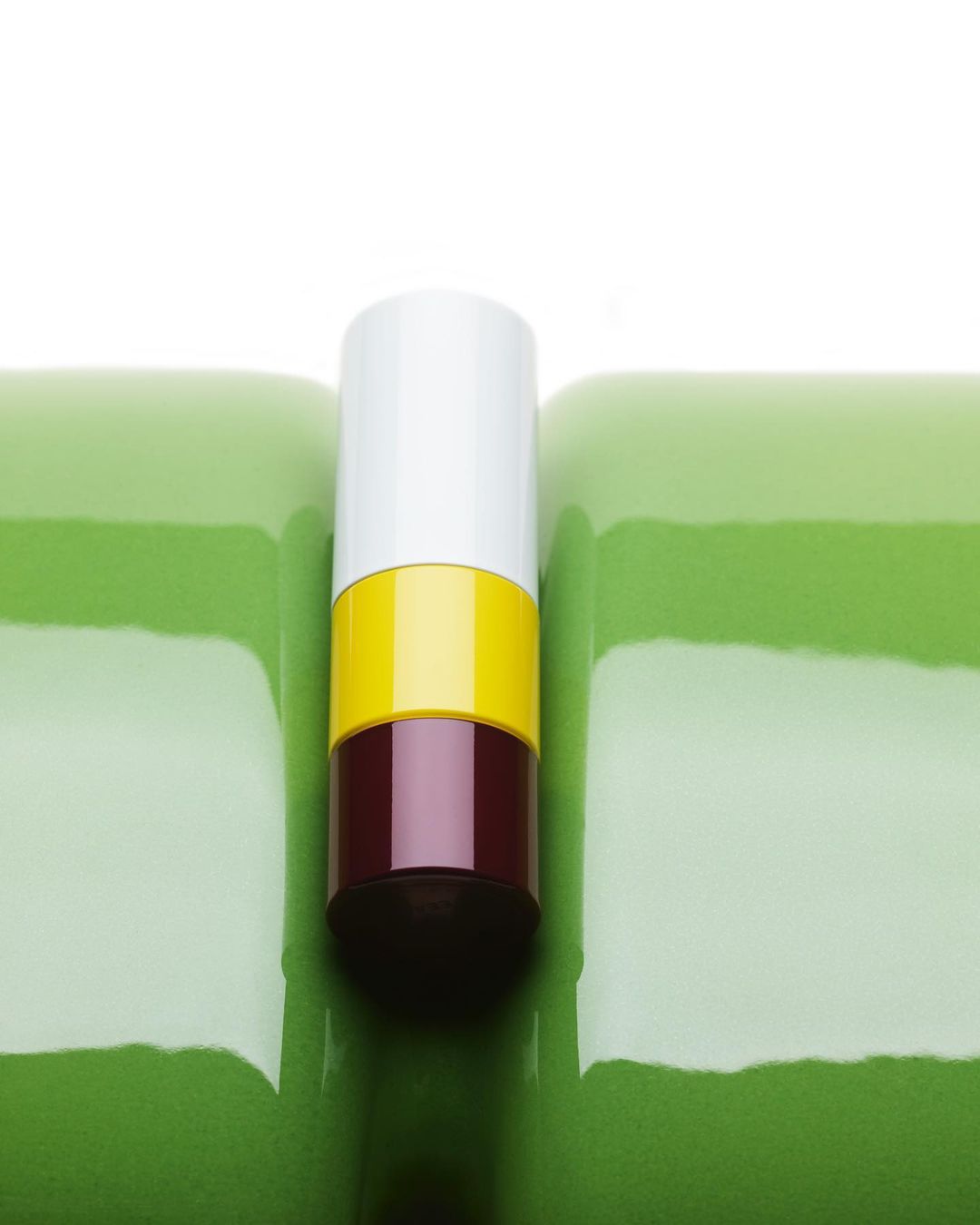 Close-up of a vertically stacked container with white, yellow, and brown sections sitting atop a green textured surface in a studio setting.