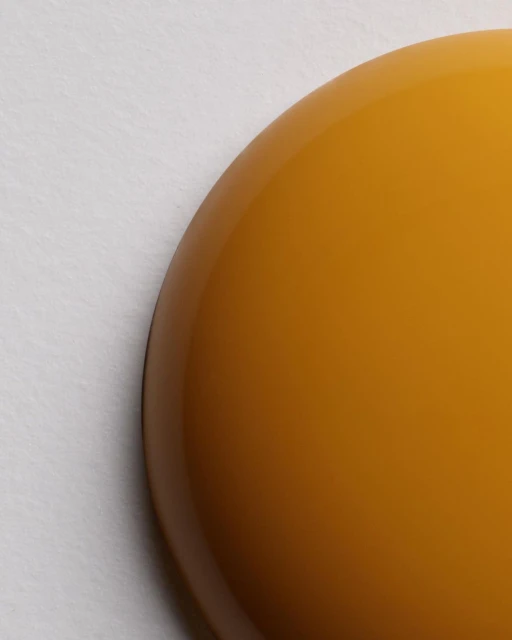 Close-up of a dome-shaped, glossy, golden-brown object against a textured off-white surface, showcasing reflections and smooth gradients.