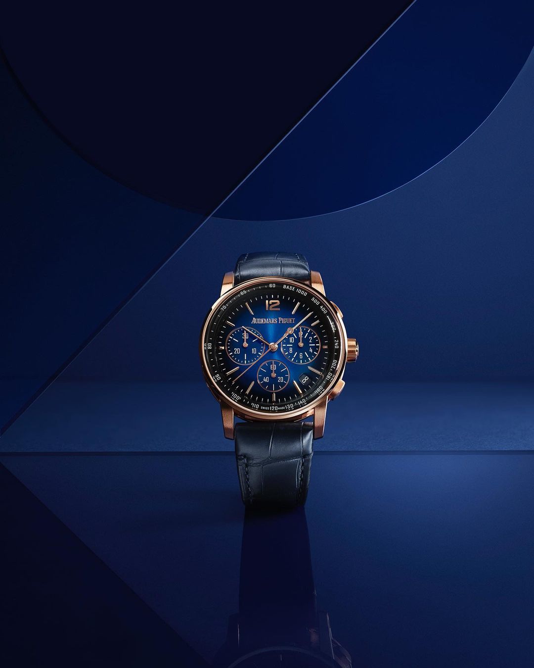 Elegant rose gold and blue Audemars Piguet wristwatch displayed on a reflective blue surface in a studio setting, product photography.